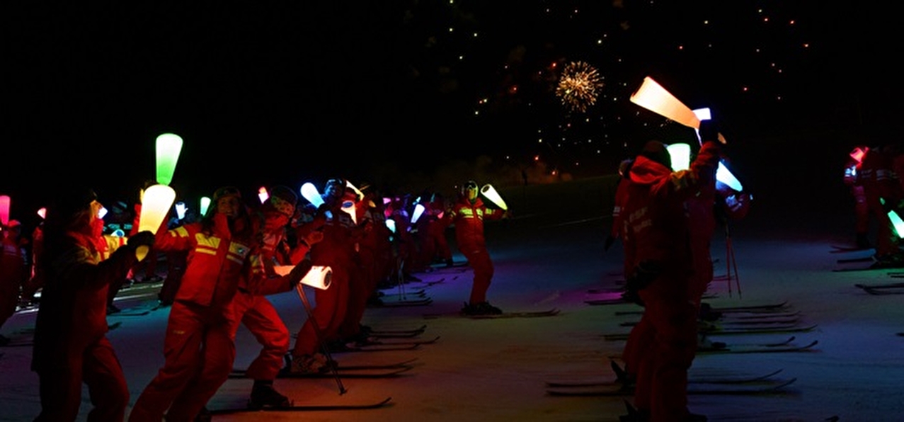 Moniteurs de ski dans la nuit avec des flambeaux lumineux en main