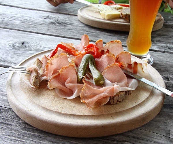 Tartine de pain posée sur une planche où sont entreposés jambon de montagne, cornichons et condiments