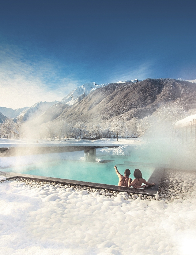 Un couple se relaxant dans un jacuzzi extérieur, avec de la neige tout autour, créant une atmosphère chaleureuse et romantique.