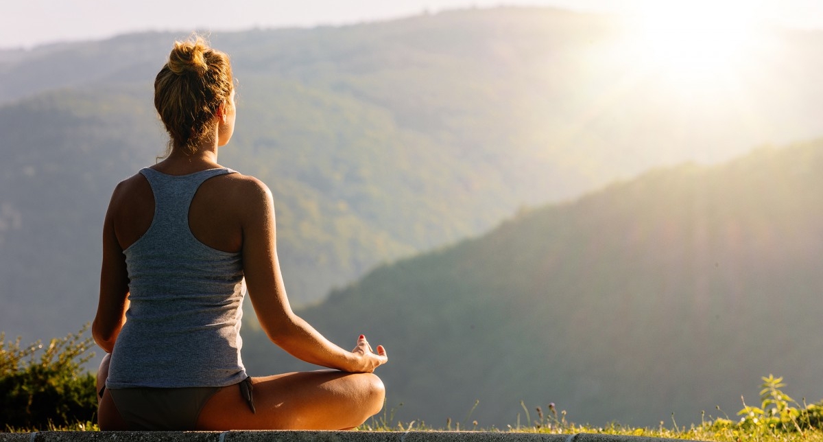 Personne en position de lotus effectuant une séance de yoga en pleine nature face aux montagnes ensoleillées