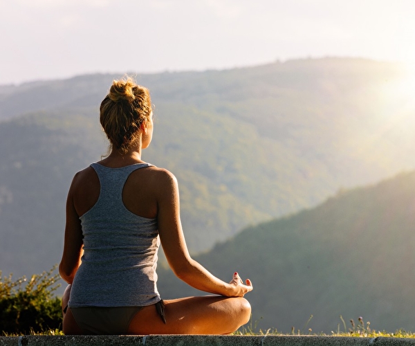 Personne en position de lotus effectuant une séance de yoga en pleine nature face aux montagnes ensoleillées