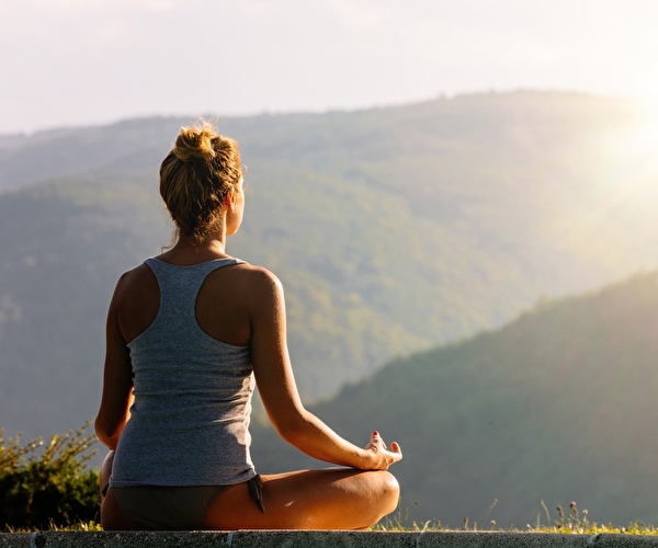 Personne en position de lotus effectuant une séance de yoga en pleine nature face aux montagnes ensoleillées