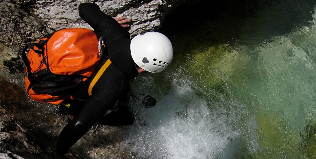 Personne équipée d'un casque et d'un sac à dos hermétique effectuant une descente en canyoning dans l'eau