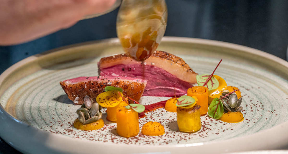 Assiette de dégustation proposant un plat fait de magret de canard tranché, de petits légumes taillés et drapé d'un assaisonnement salé