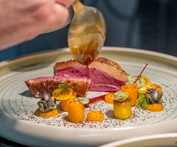 Assiette de dégustation proposant un plat fait de magret de canard tranché, de petits légumes taillés et drapé d'un assaisonnement salé