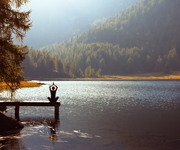 Personne en position assiste sur un ponton près d'un lac effectuant une séance de yoga face à la nature et aux montagnes