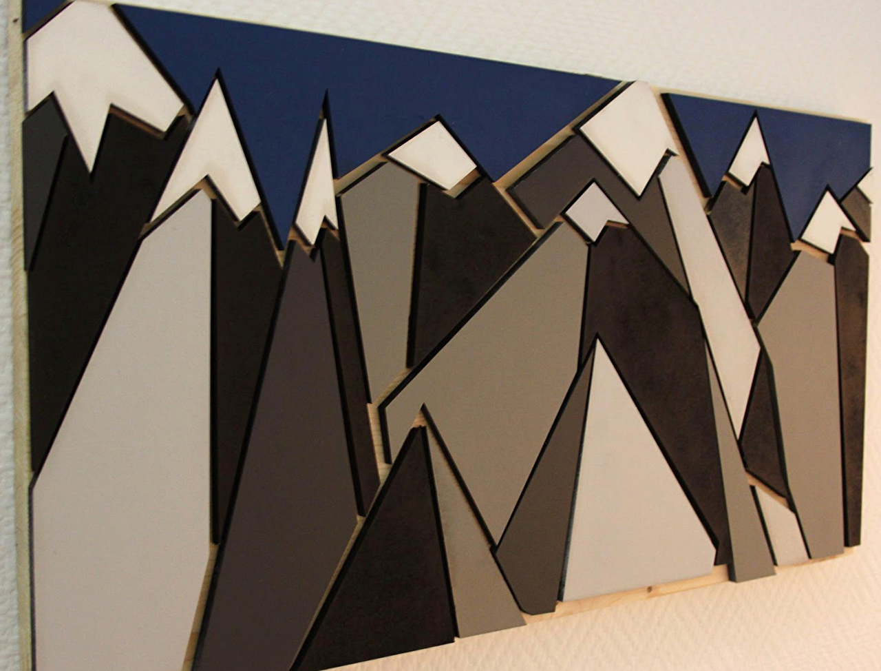 Oeuvre d'art alliant géométrie, graphisme et montagnes enneigées en bois sur une toile panoramique