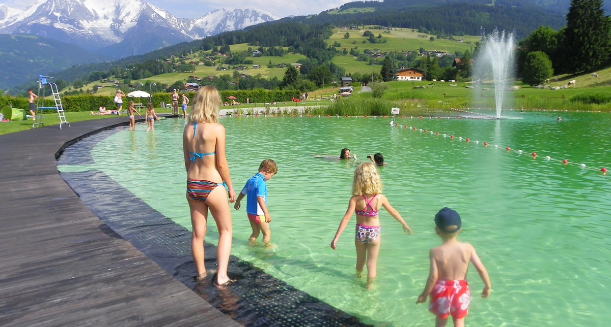 Jeunes enfants en maillots de bain rentrant dans un plan d'eau entouré d'une terrasse en bois en montagne l'été