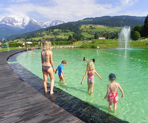 Jeunes enfants en maillots de bain rentrant dans un plan d'eau entouré d'une terrasse en bois en montagne l'été