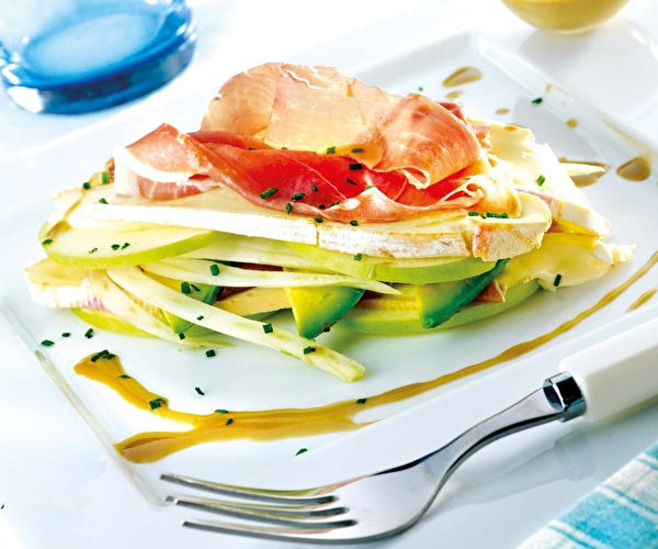 Présentation d'un mille-feuilles fraîcheur avec des lamelles de pomme, du fromage et du jambon de montagne sur une assiette blanche