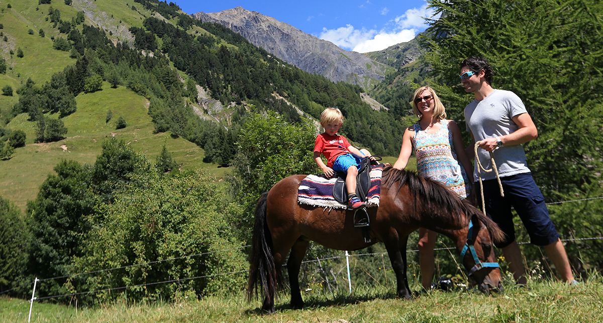 Couple de parents avec leur enfant monté sur le dos d'un poney en balade au coeur de la montagne l'été