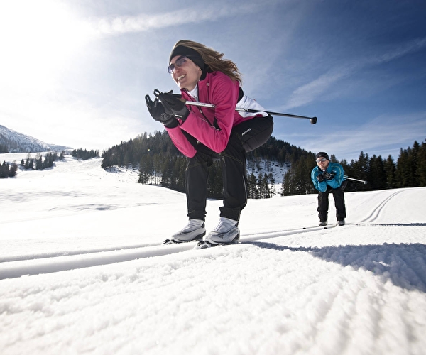 Personnes effectuant une descente en ski de fond sur une piste bordée de sapins en montagne l'hiver