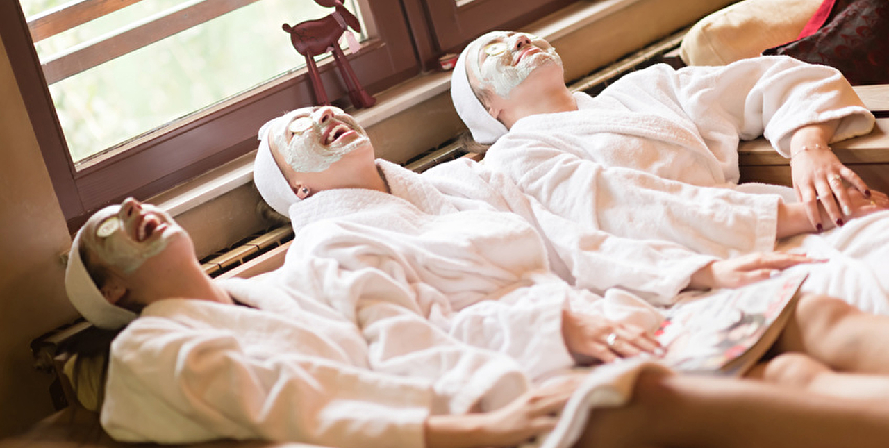 Personnes allongées dans un canapé en peignoirs avec un masque cosmétique sur le visage et des concombres sur les yeux
