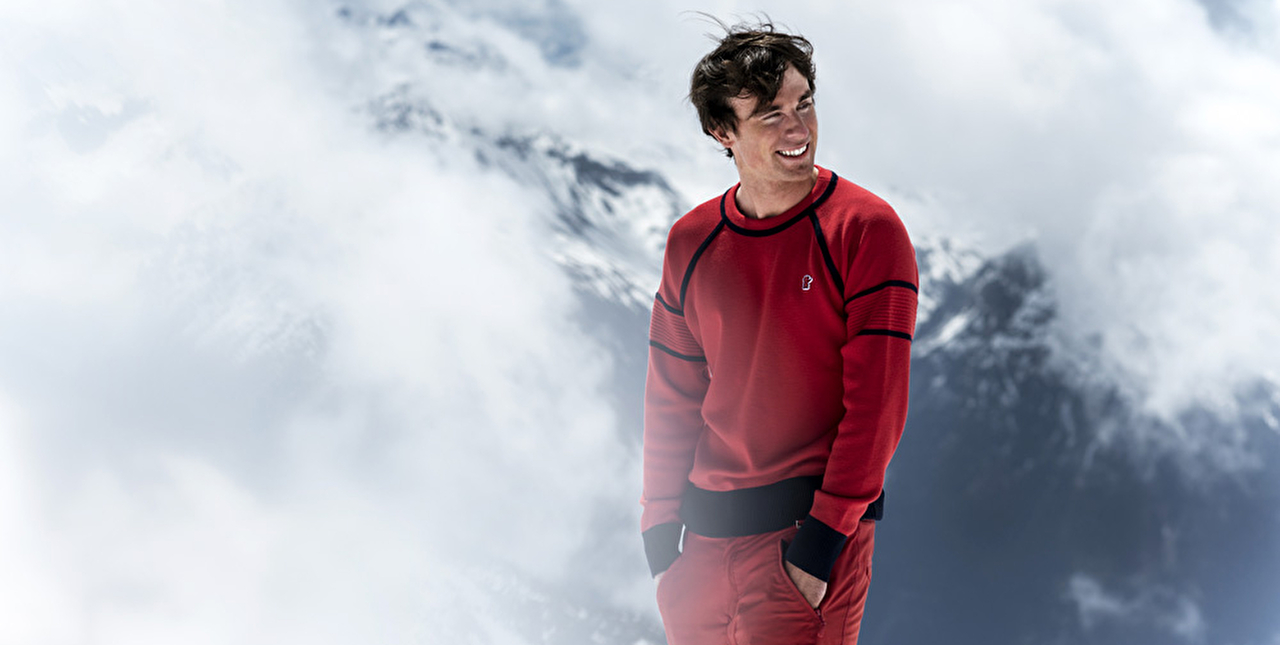 Vue d'une personne équipée d'un pull rouge et d'un pantalon de ski en haute montagne à travers les nuages