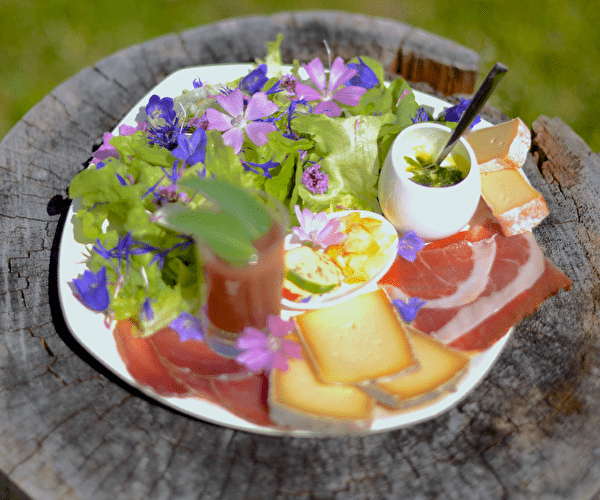 Assiette gourmande à base de jambon fumé, fromages, fleurs et plantes de montagne accompagnée de petites sauces