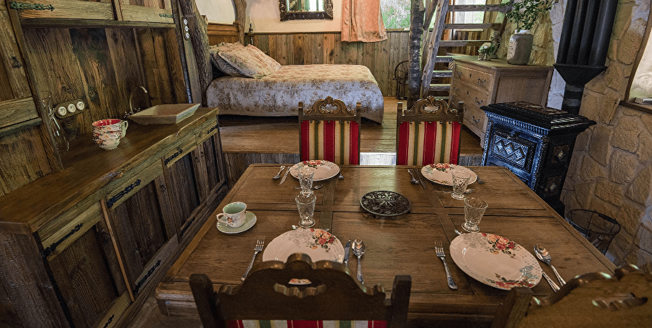Intérieur d'un chalet en bois et pierres avec chambre à coucher et espace cuisine avec sa table dressée