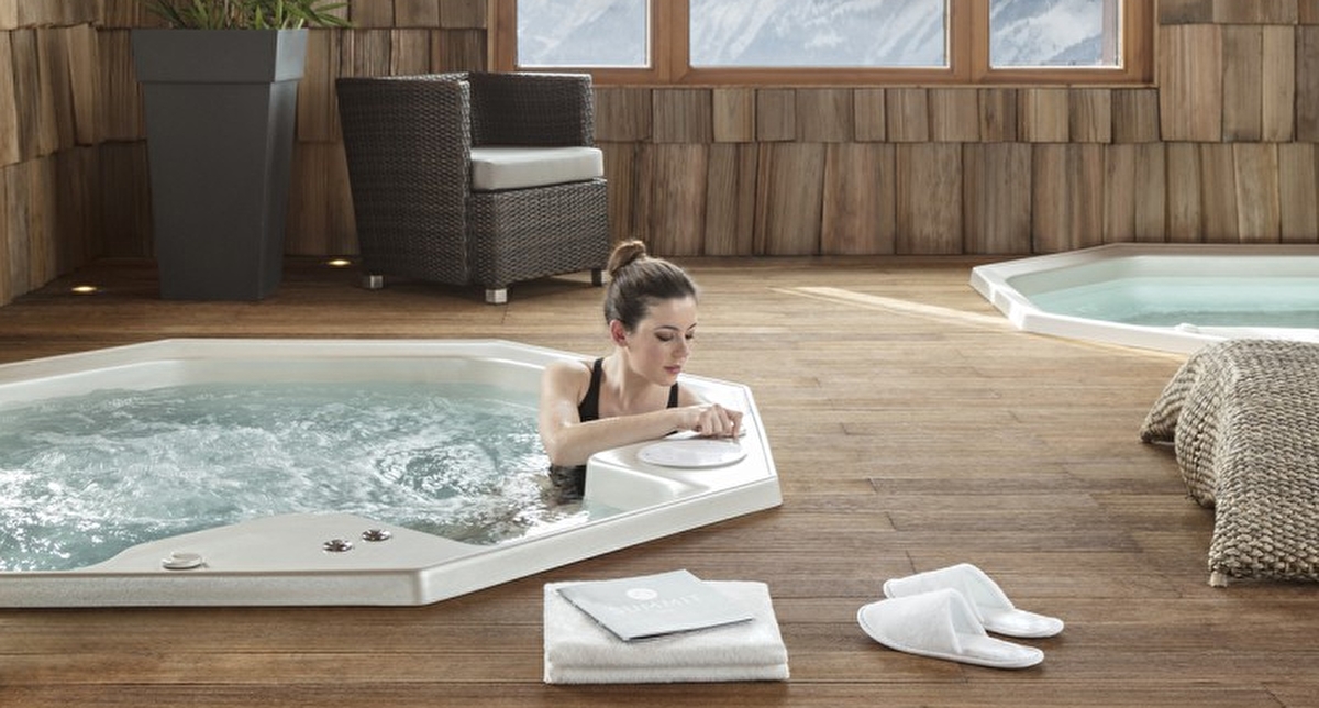 Intérieur d'un spa en bois avec plusieurs jacuzzis de relaxation face aux montagnes l'hiver