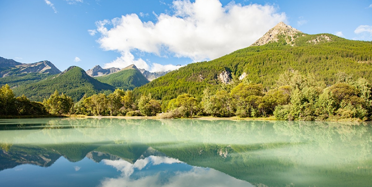 Vue sur un lac de montagne entouré de verdure et des montagnes environnantes