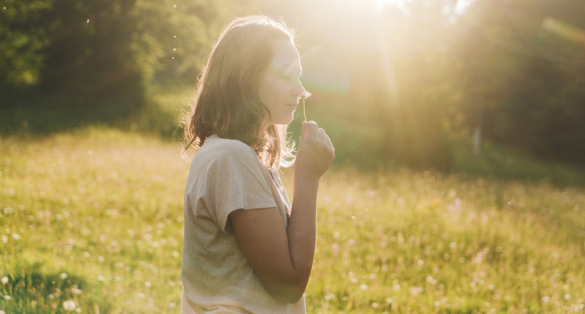 Personne reniflant une fleur les yeux fermés en pleine nature l'été sous le soleil