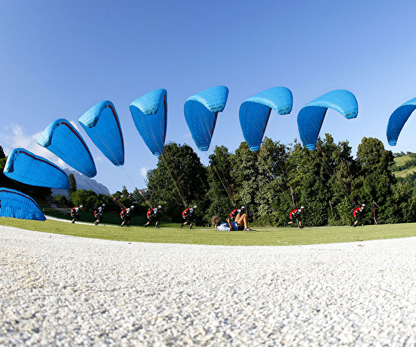 groupe de personnes équipées d'une voile de parapente dans une vallée effectuant des manoeuvres
