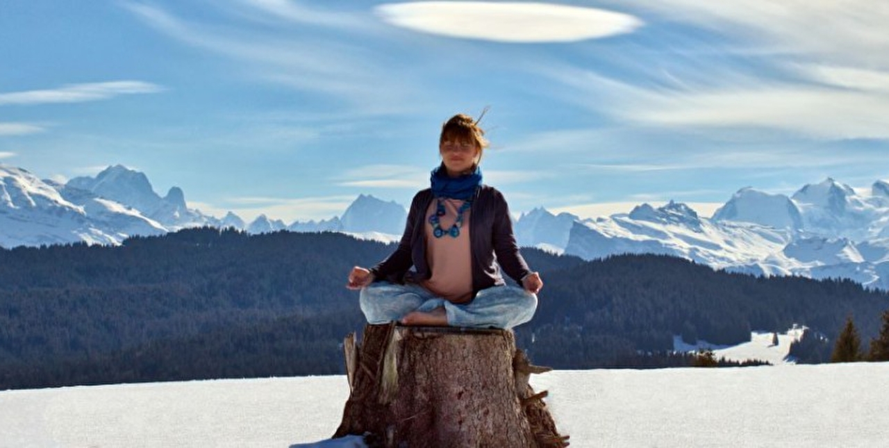 Personne effectuant une posture de yoga assise sur un tronc face aux montagne l'hiver