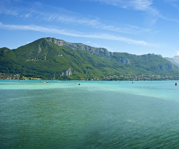 Vue sur un lac aux couleurs turquoise entouré de montagnes sur lequel sont amarrés des bateaux à moteur