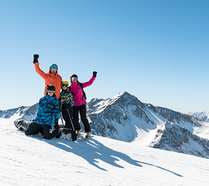 Famille en haut des pistes levant les bras au ciel devant un paysage de montagne