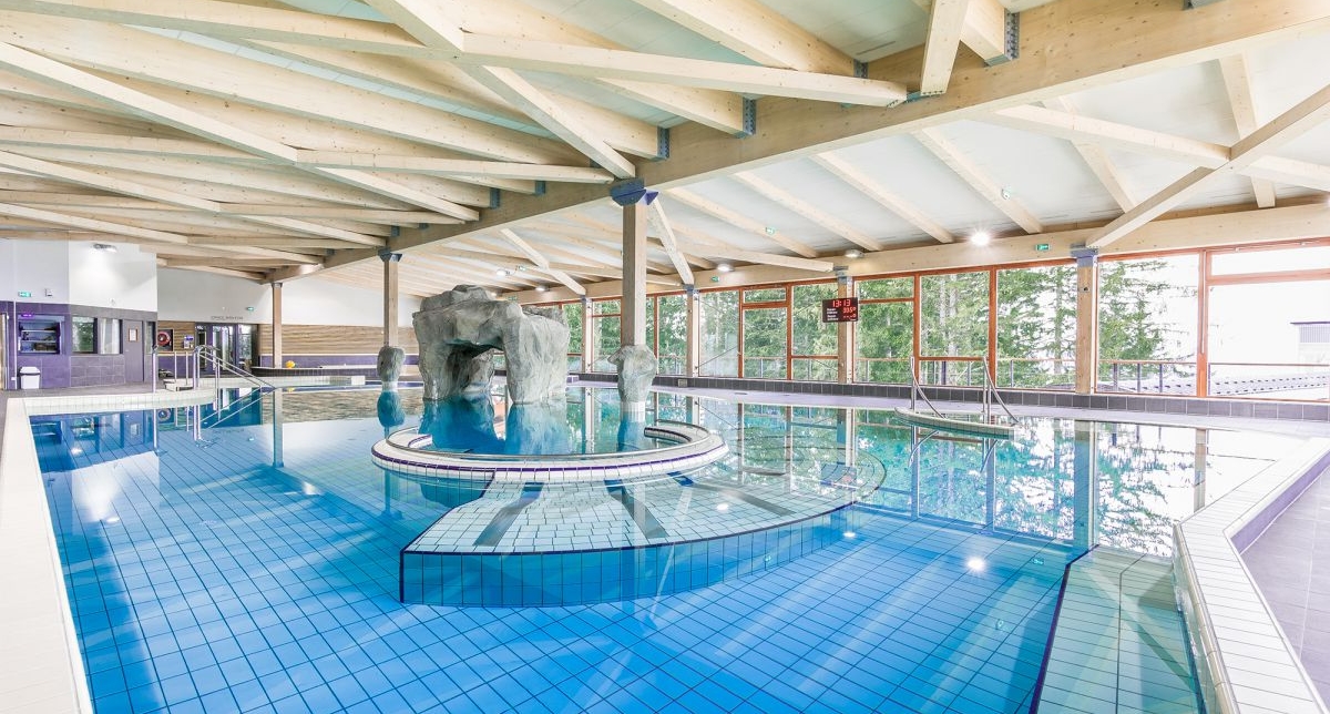Vue sur la piscine intérieure d'un centre aqualudique ouvert par de larges vitres sur l'extérieur