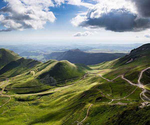 Vue panoramique sur des vallées et montagnes verdoyantes où serpentent de petits chemins de randonnées
