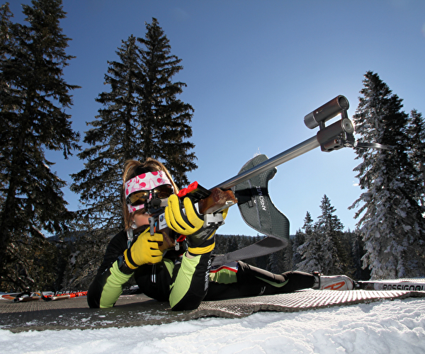 Personne en position allongée tenant sa carabine lors d'une séance de biathlon en montagne l'hiver