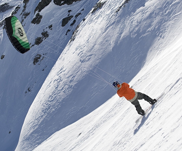 Personne équipée d'une planche de snowboard et d'une voile de kite effectuant une descente de piste enneigée