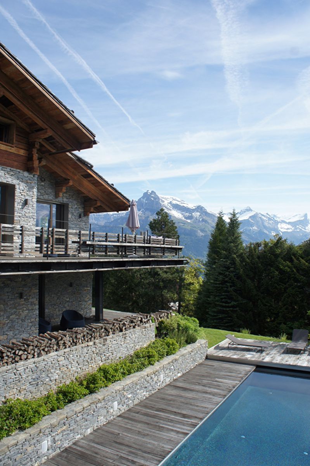 Vue sur une habitation de montagne avec balcon, piscine et coin terrasse face à la montagne enneigée