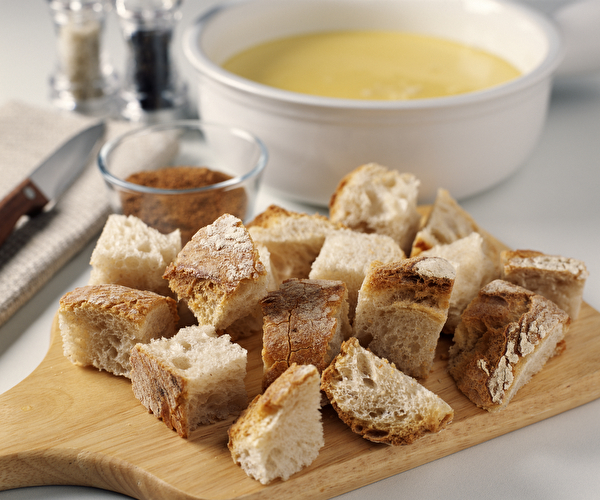 Présentation d'une fondue savoyarde avec ses morceaux de pain proposés sur une planche en bois