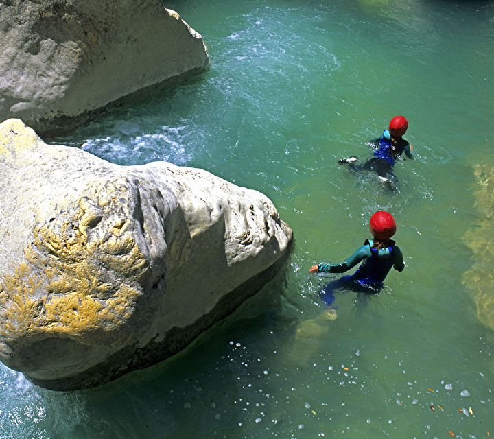 Personnes équipés de combinaisons et de casques dans l'eau lors d'une activité canyoning l'été