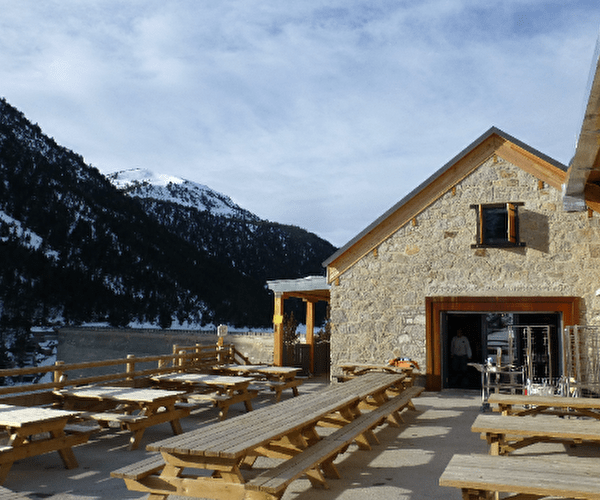 Vue sur un refuge de montagne en extérieur et sa terrasse attenante avec tables et bancs