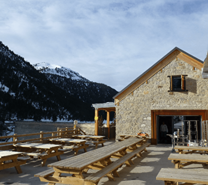 Vue sur un refuge de montagne en extérieur et sa terrasse attenante avec tables et bancs