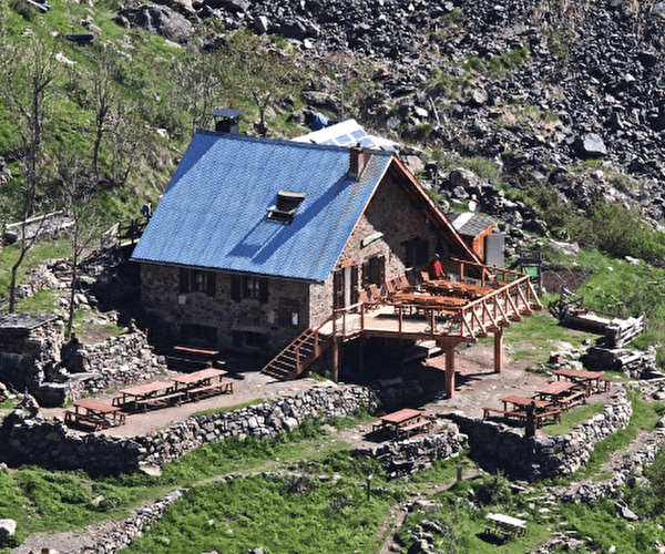 Vue sur un refuge de montagne en bois avec une terrasse en hauteur en pleine montagne l'été