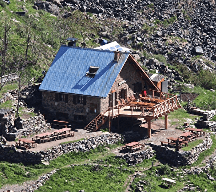 Vue sur un refuge de montagne en bois avec une terrasse en hauteur en pleine montagne l'été