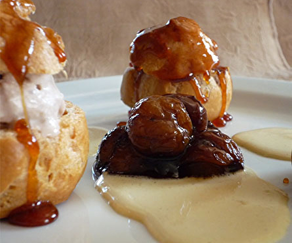 Profiteroles dressées dans une assiette avec son lit de crème anglaise agrémenté de châtaignes