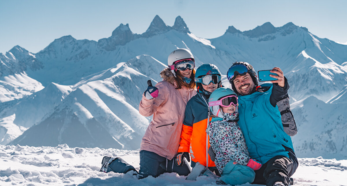 Famille prenant un selfie assis dans la neige sur les pistes