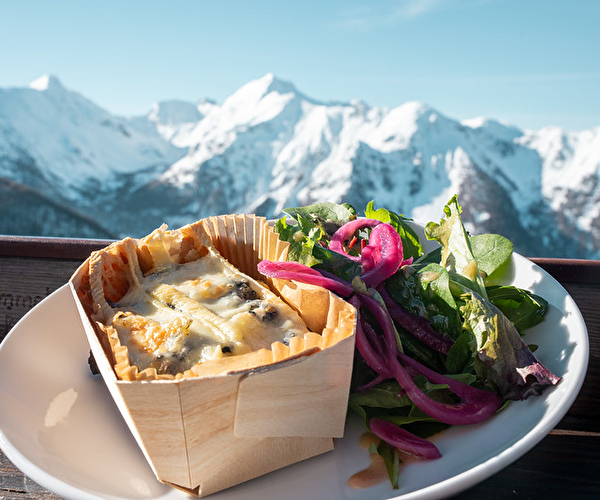 Plat à base de fromage posé sur le rebord d'une table avec vue sur les sommets enneigés