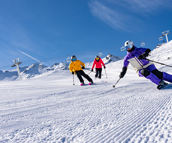 3 skieurs dévalant les pistes sous un grand ciel bleu