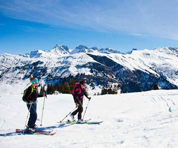 Personnes effectuant du ski de rando en pleine nature face aux sommets enneigés