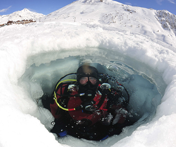 Personne effectuant une plongée sous glace avec les équipements adaptés en montagne l'hiver