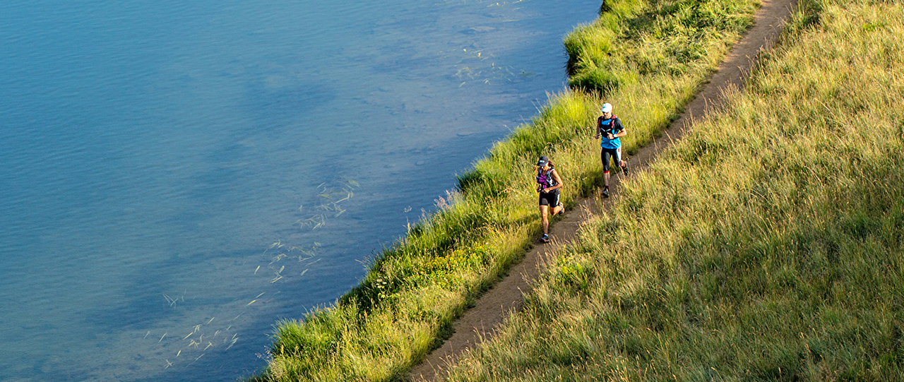 Personnes effectuant une course trail sur un chemin près de l'eau en montagne l'été