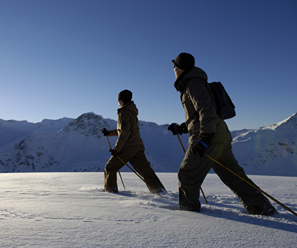 Personnes effectuant de la marche nordique dans une épaisse couche de neige face aux montagnes enneigées sous le soleil