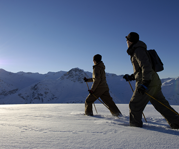 Personnes effectuant de la marche nordique dans une épaisse couche de neige face aux montagnes enneigées sous le soleil