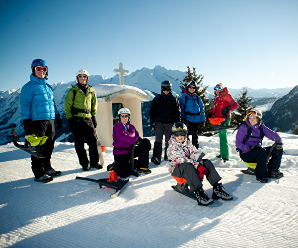 Groupe de personnes équipés de yooner en haut d'une montagne proche d'une chapelle prêts à descendre une piste de ski