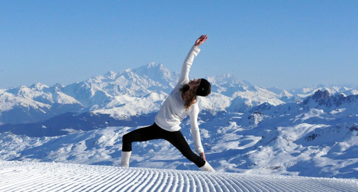 Personne effectuant une posture de yoga en tenue de ski en haut de la montagne l'hiver