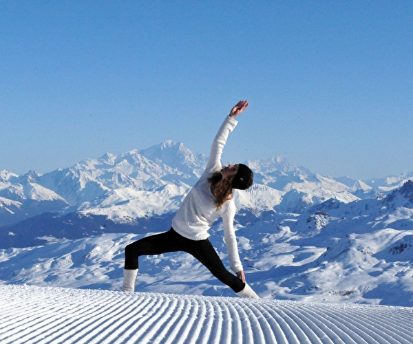 Personne effectuant une posture de yoga en tenue de ski en haut de la montagne l'hiver